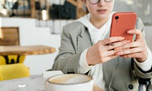 A woman sits at a cafe table and looks at her phone.