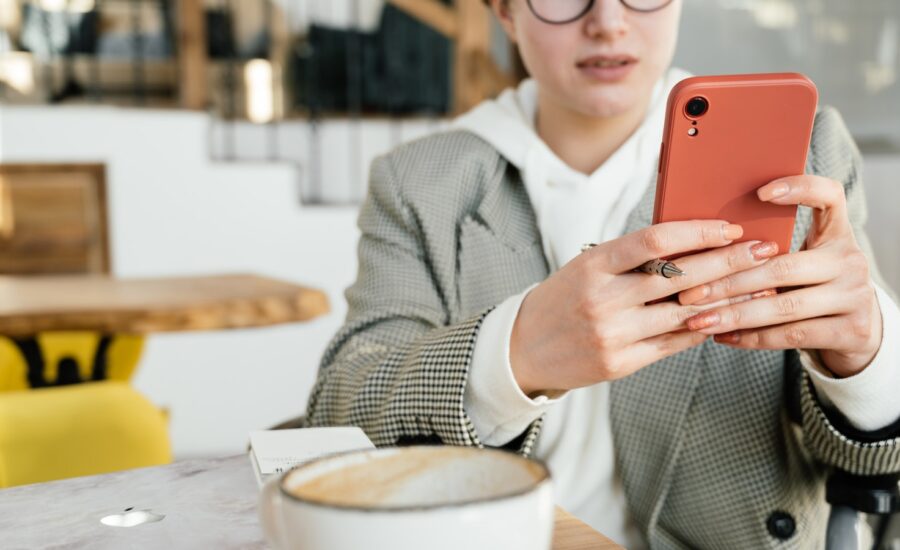 A woman sits at a cafe table and looks at her phone.