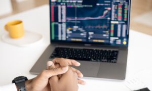 A pair of clasped hands in front of a laptop displaying a graph.