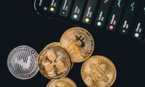 Several coins with cryptocurrency logos next to a cellphone.