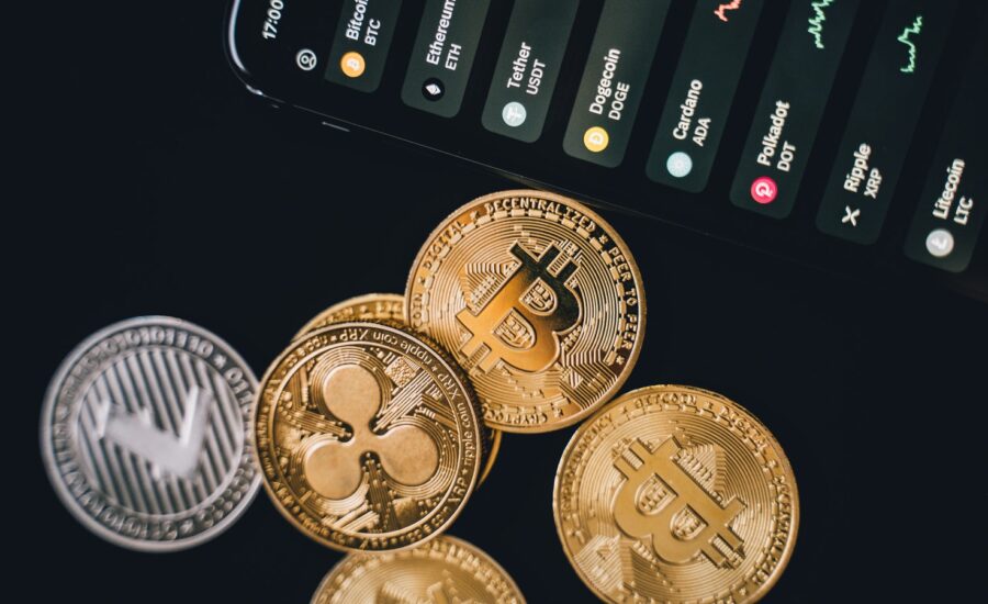 Several coins with cryptocurrency logos next to a cellphone.