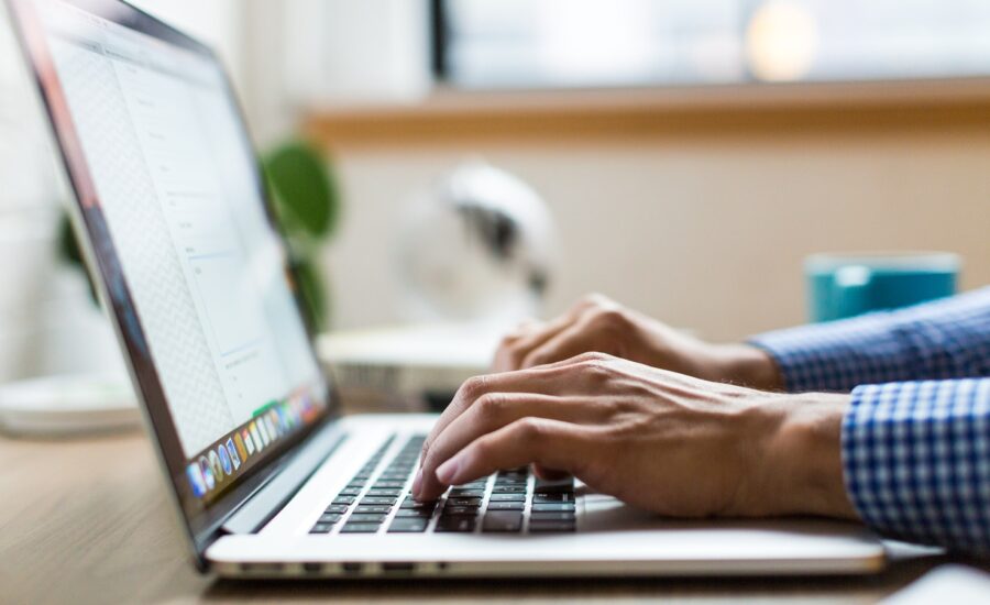 A pair of hands types on a laptop keyboard shown from the side.