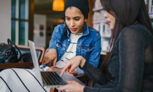 Two women study and point at a laptop screen.