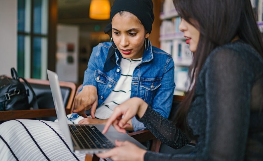 Two women study and point at a laptop screen.