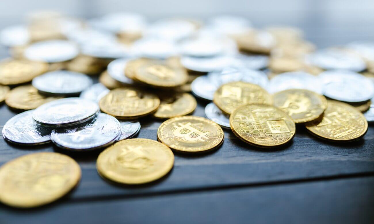 A pile of gold and silver coins with cryptocurrency logos.