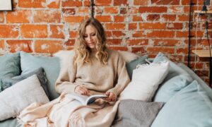 A women sits on a couch and reads a book.