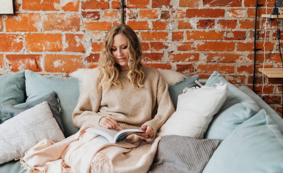 A women sits on a couch and reads a book.