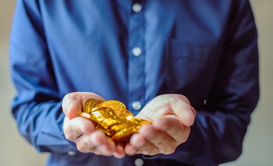 A man's hands hold a pile of shiny gold coins.