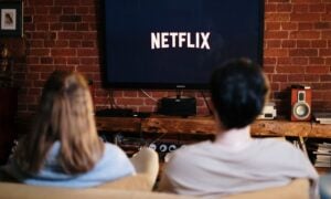 A couple is seen sitting on a sofa looking at a TV with it displaying Netflix logo