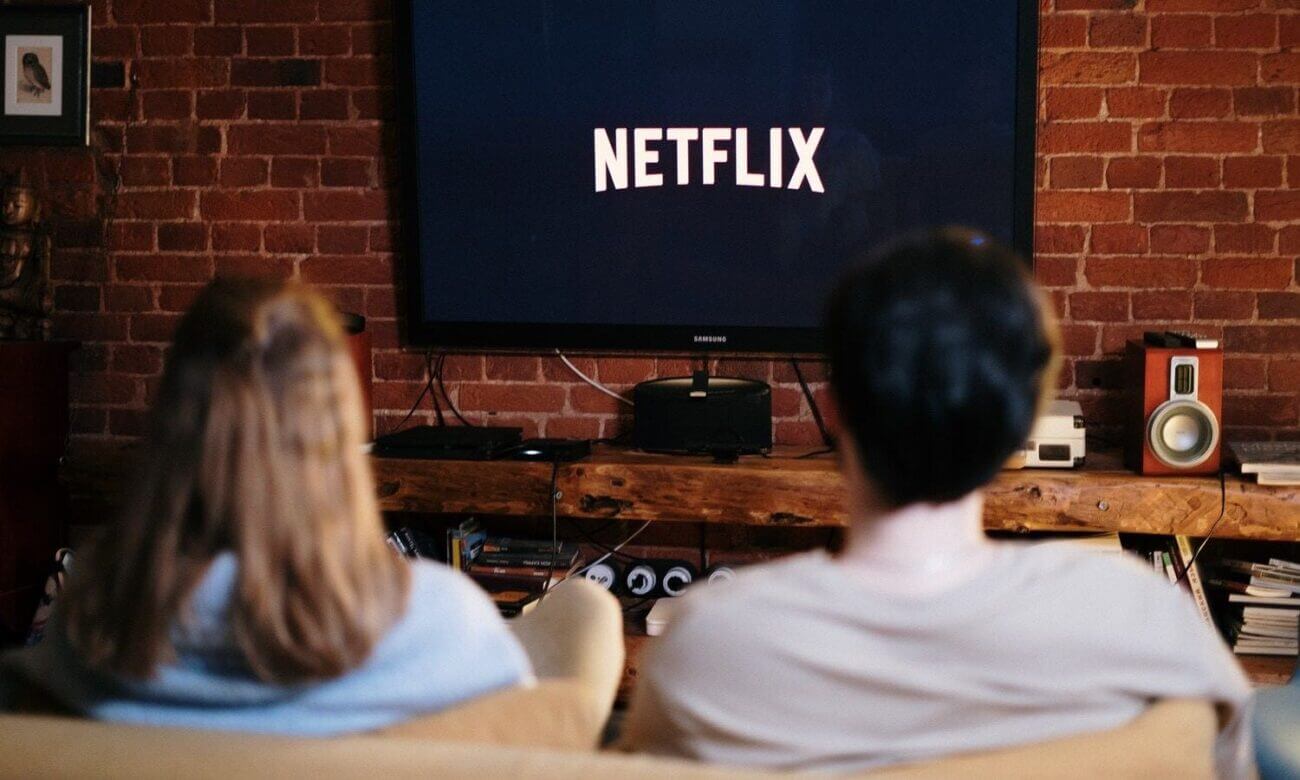 A couple is seen sitting on a sofa looking at a TV with it displaying Netflix logo
