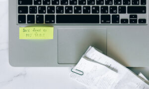 a computer with receipts on a table, with a stick note saying, "Don't forget to do you your taxes."