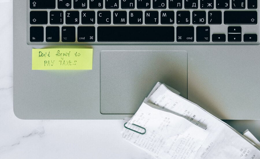 a computer with receipts on a table, with a stick note saying, "Don't forget to do you your taxes."