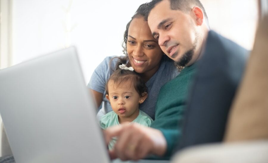 A mom, dad and baby girl with Down syndrome looking at a laptop together.