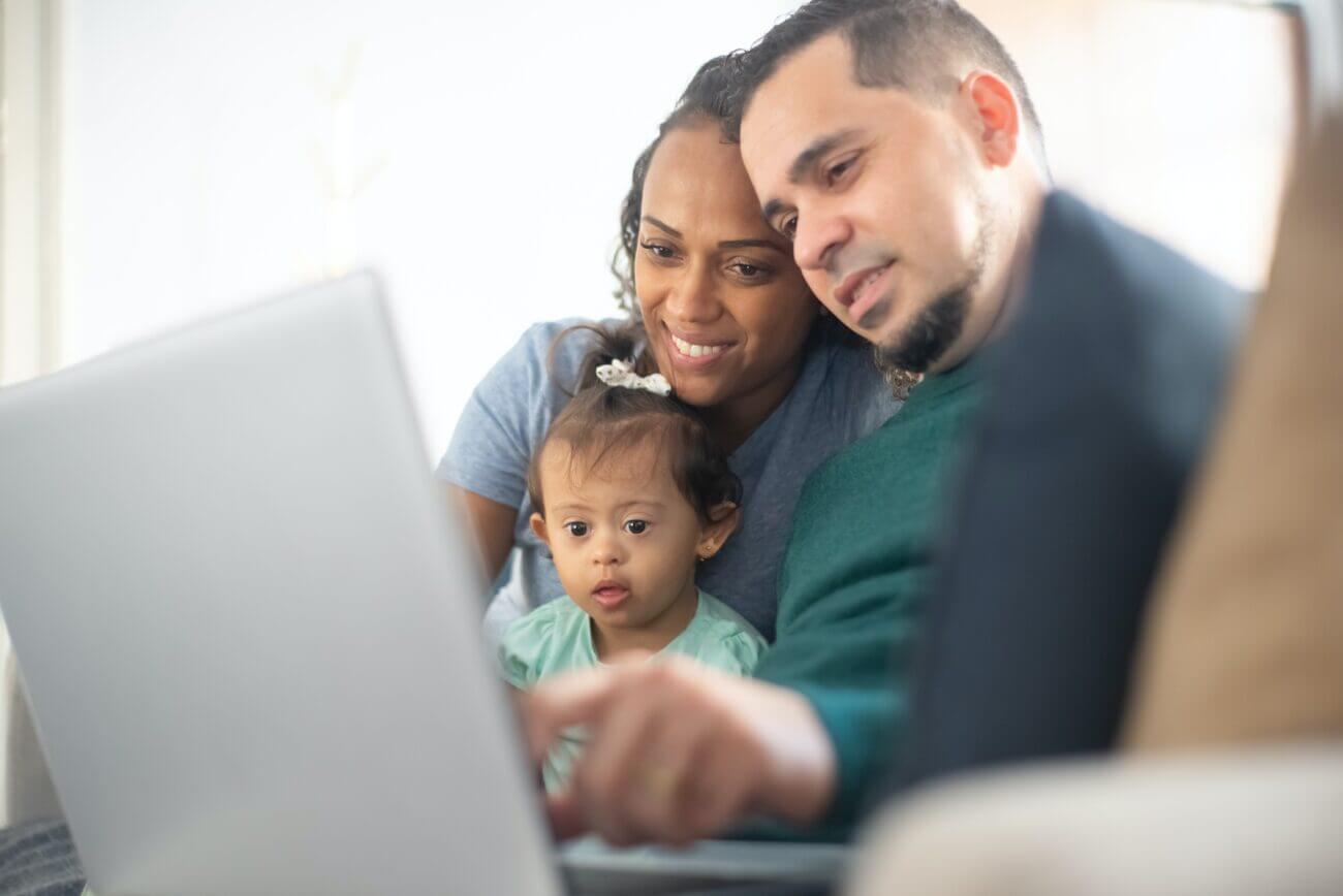 A mom, dad and baby girl with Down syndrome looking at a laptop together.
