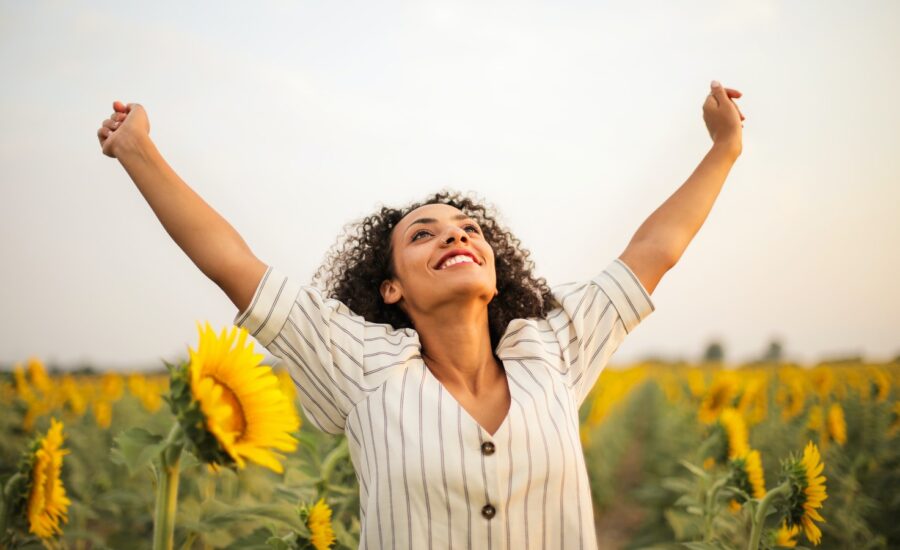 A happy woman with outstretched arms in a field of sunflowers.