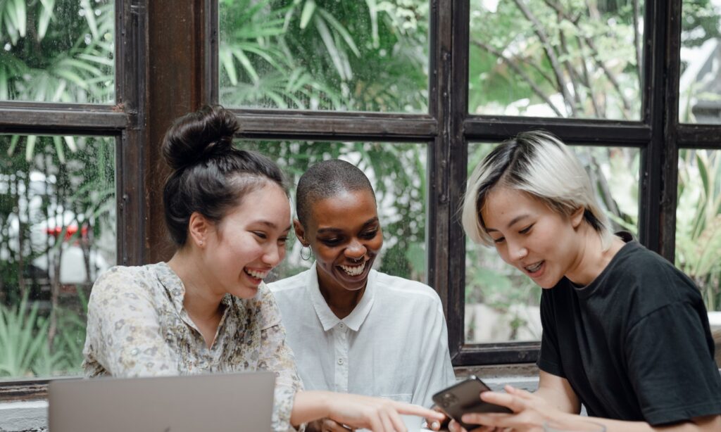 three young women in cafe talking over laptop