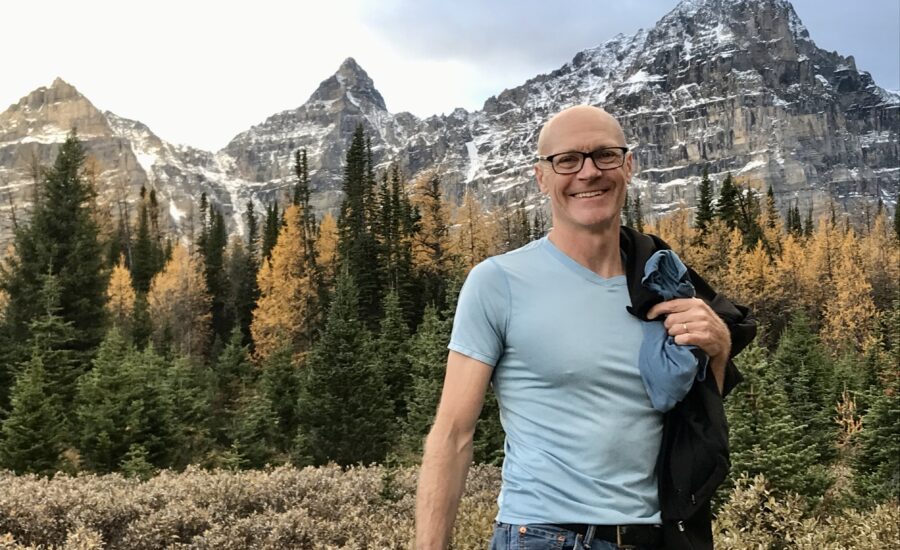 Andrew Hallam stands in front of a mountain and forest.