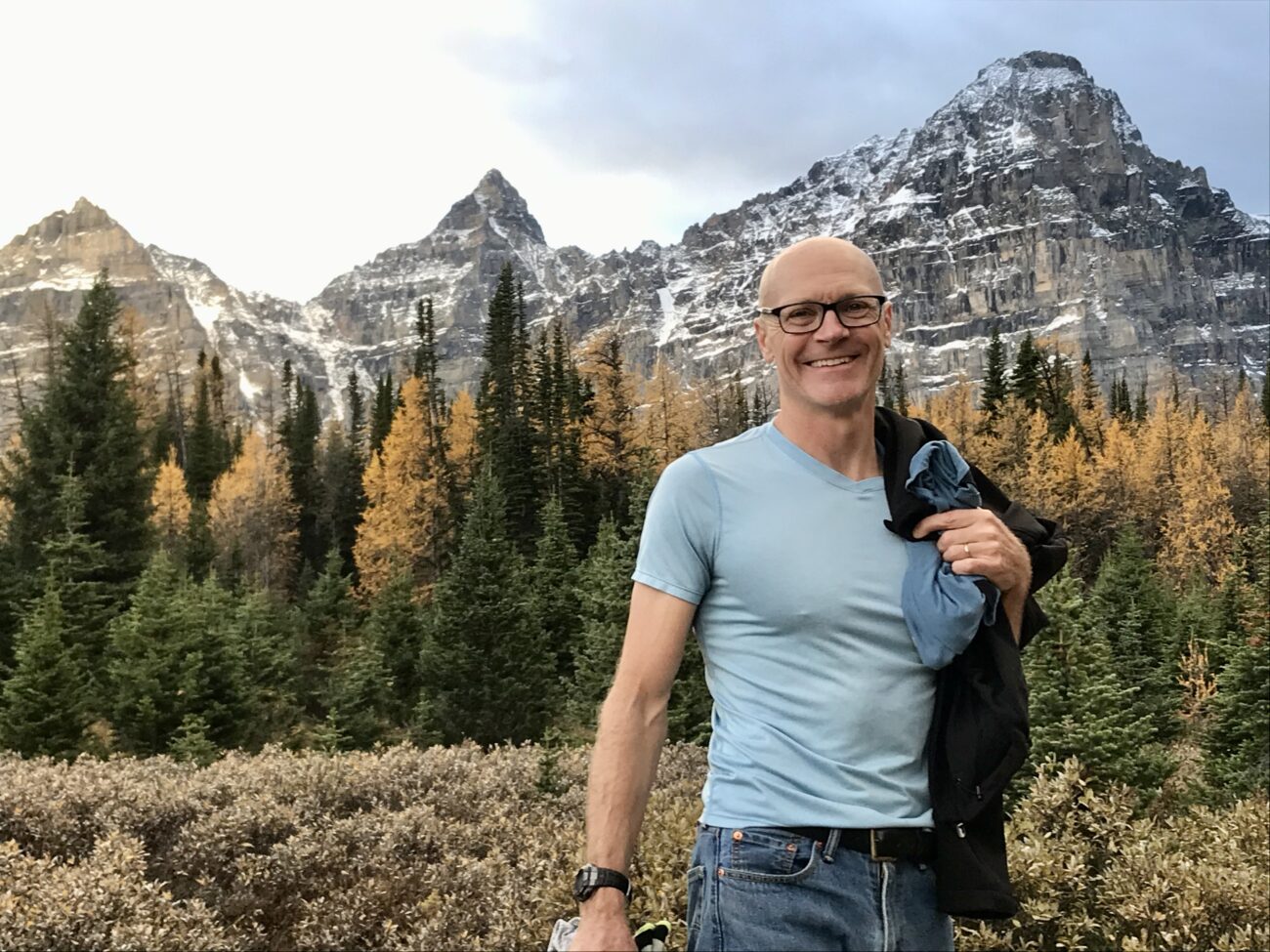 Andrew Hallam stands in front of a mountain and forest.