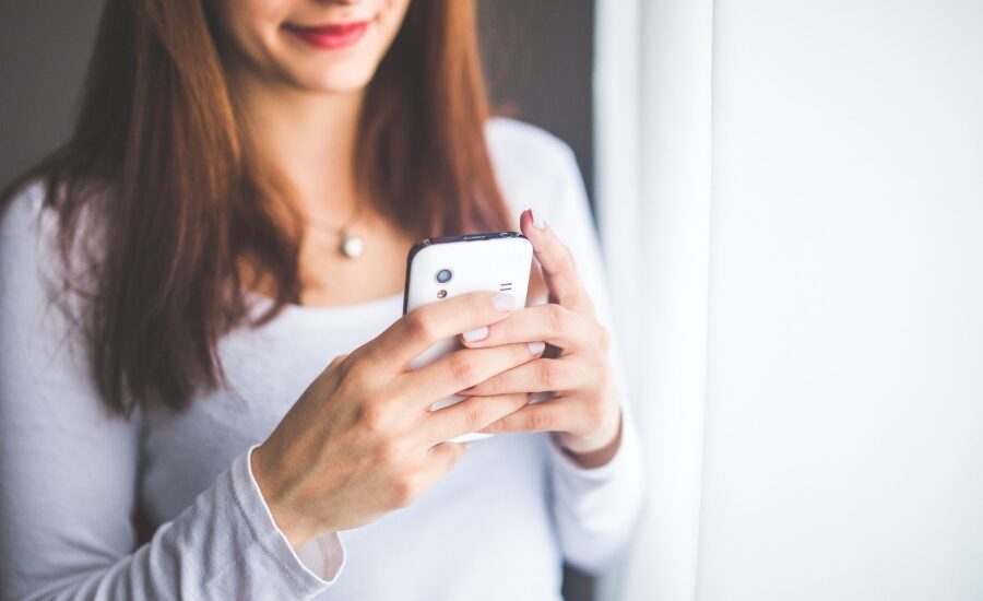 A smiling woman looks down at her smartphone.