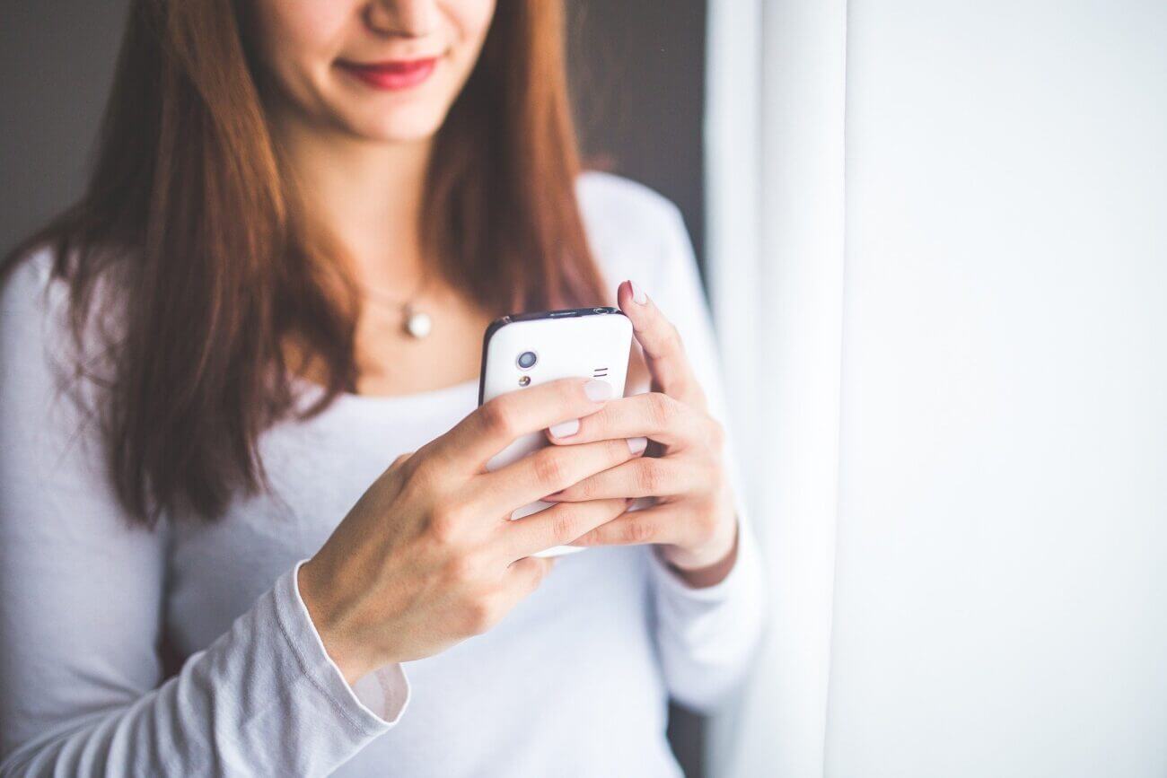 A smiling woman looks down at her smartphone.