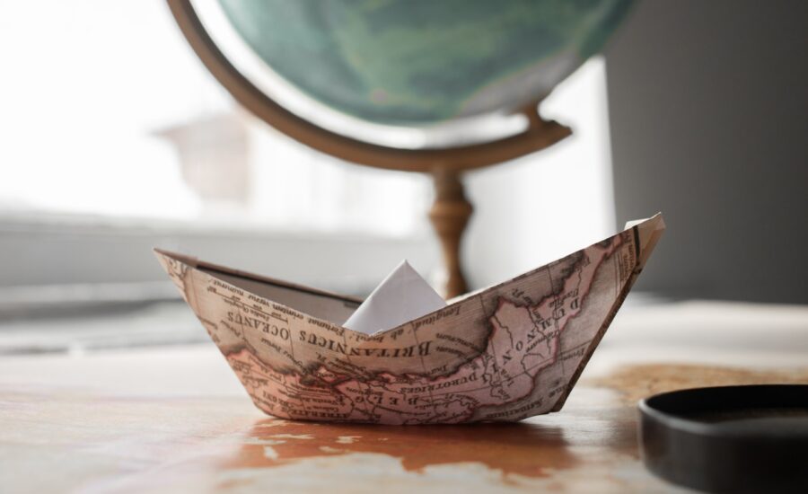 An origami boat made from a map sits in front of a globe.