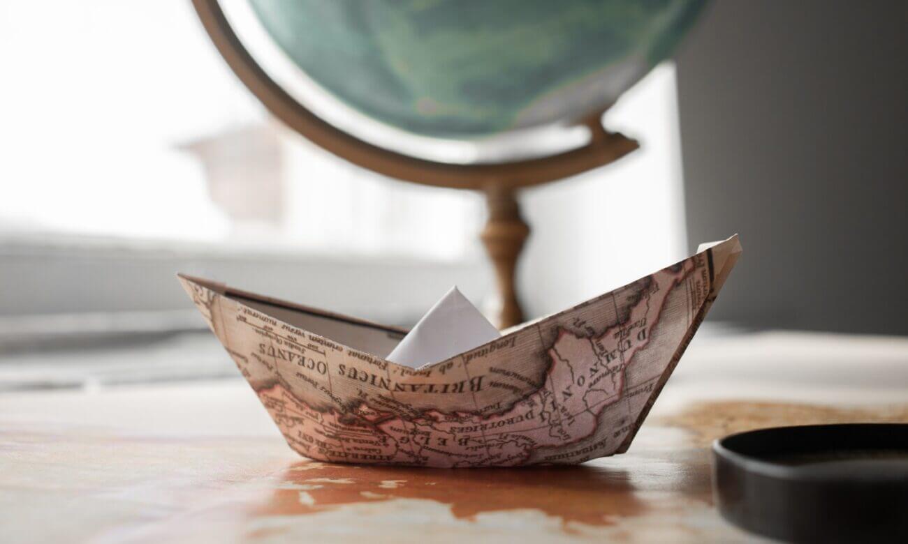 An origami boat made from a map sits in front of a globe.