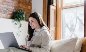 A smiling woman looks at her laptop.