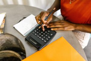 a woman sits at a table calculating expenses with calculator, folders and paper