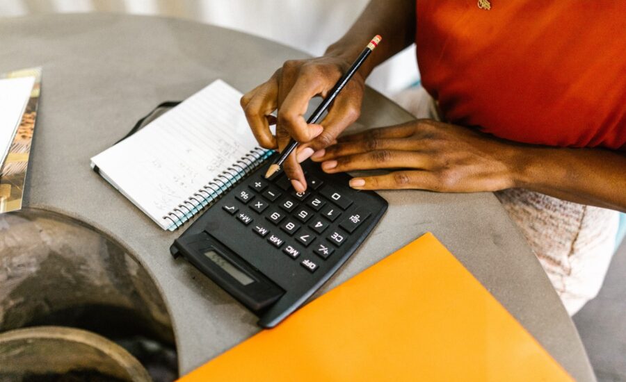 a woman sits at a table calculating expenses with calculator, folders and paper