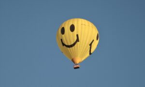 A yellow hot-air balloon with a smiley face in a cloudless blue sky