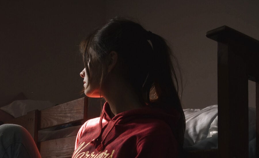 a woman sitting in a dark, cool room, with her face warmed by the sun. She's sitting on the floor, leaning her back on the bed.