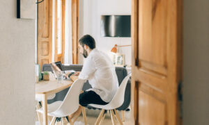 A man sits in his kitchen, looking at his RRSP statements on his laptop.