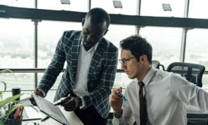 Two men in an office environment are looking at charts, discussing the ups and downs of the market