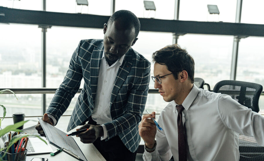 Two men in an office environment are looking at charts, discussing the ups and downs of the market