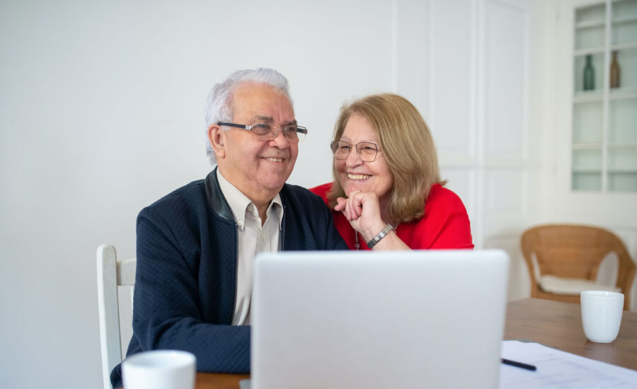 A retired couple at the table, they are smiling looking at a recent investment they just made on their computer.