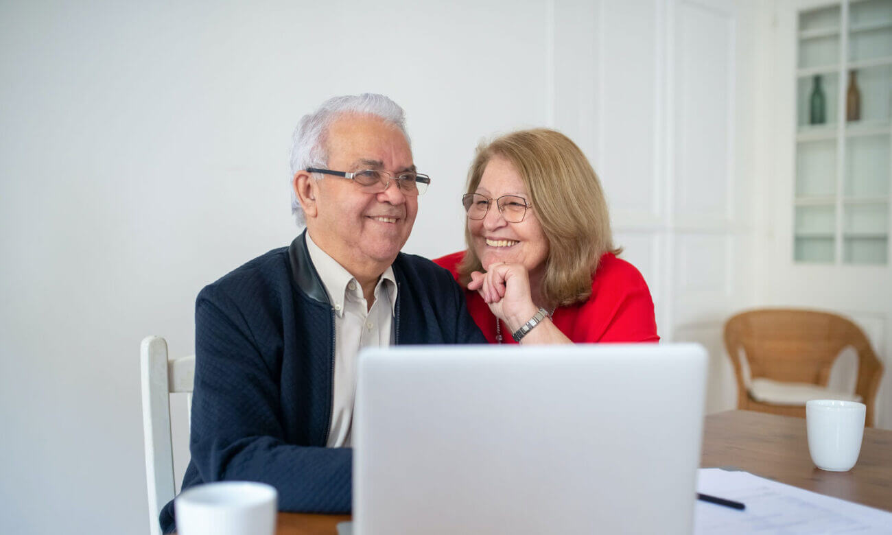 A retired couple at the table, they are smiling looking at a recent investment they just made on their computer.