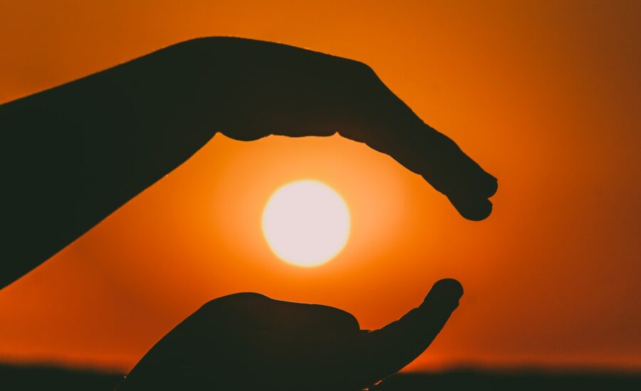 Two silhouetted hands frame a setting sun from above and below.