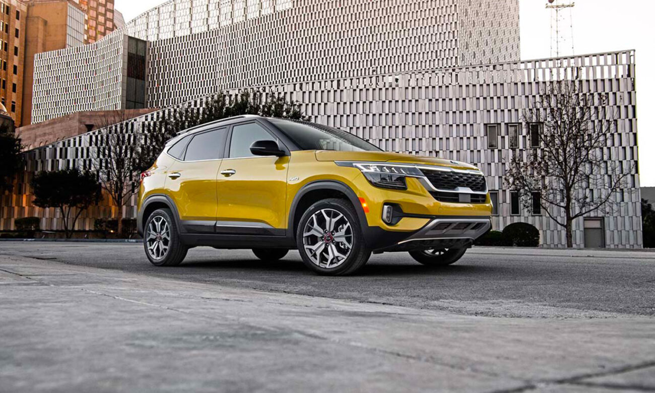 Parked on a street beside a large-bricked building, the Kia Seltos is a subcompact SUV