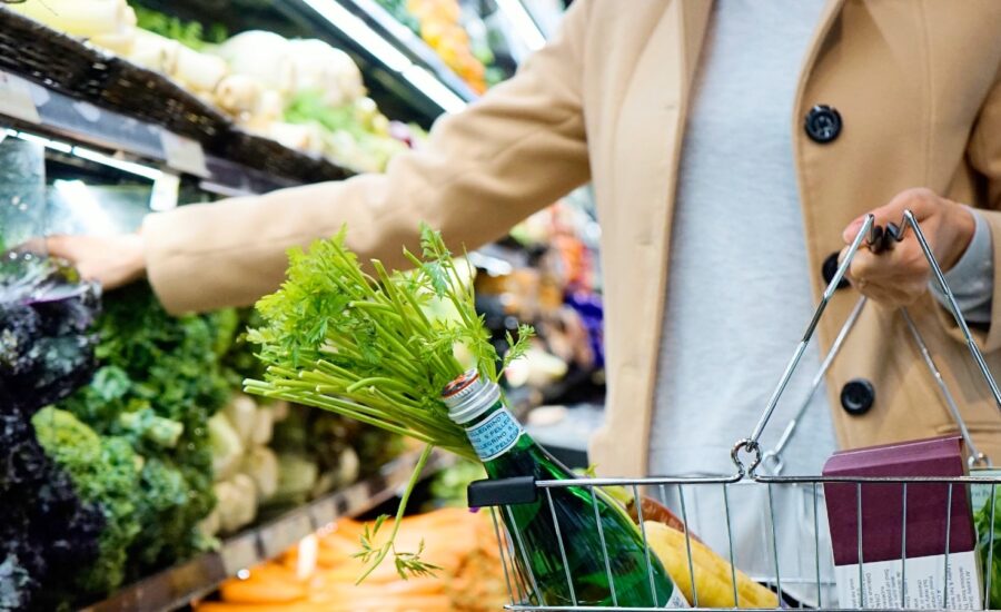 woman in peacoat reaches for produce in grocery store