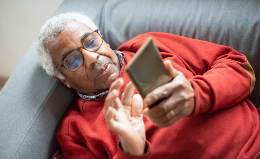 A senior-age man lies on a sofa and looks at his smartphone
