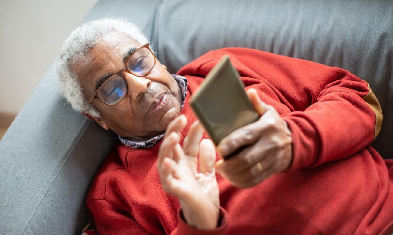 A senior-age man lies on a sofa and looks at his smartphone