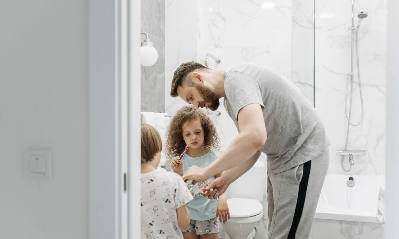 A father and his son and daughter are in the bathroom, brushing their teeth, getting ready for bed.
