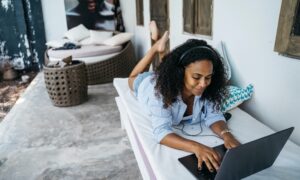 A woman is seen working on a laptop and laying down