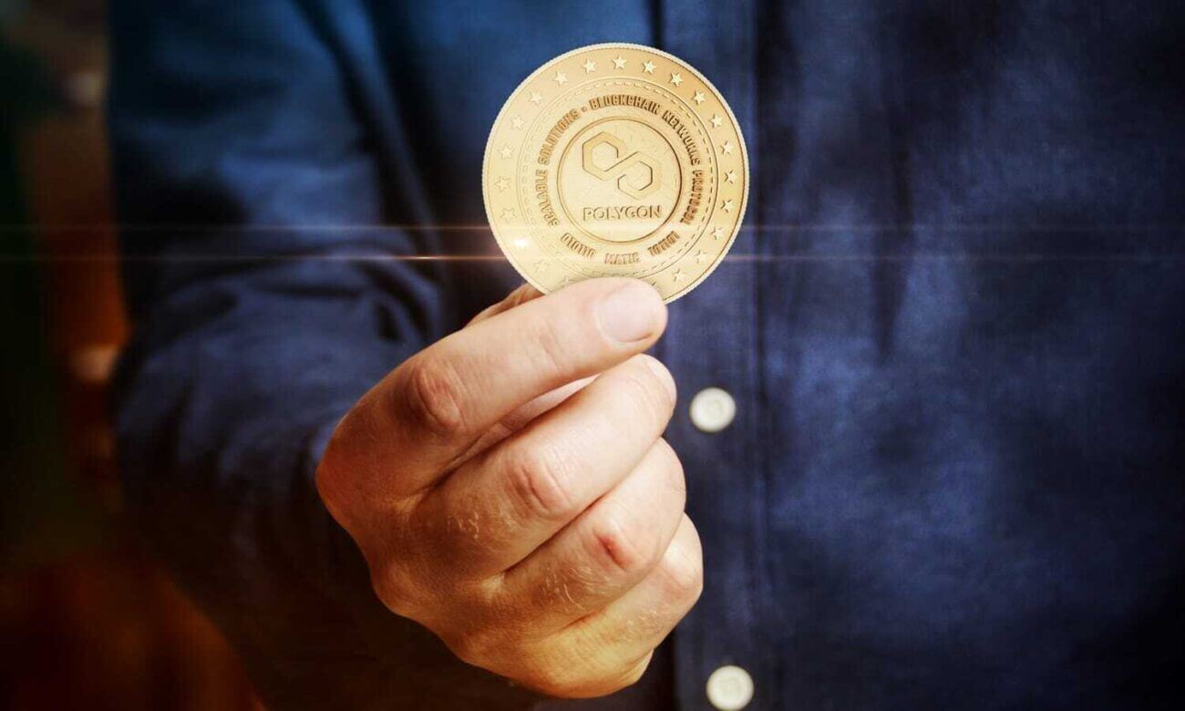 A hand holds a gold coin with the Polygon logo.