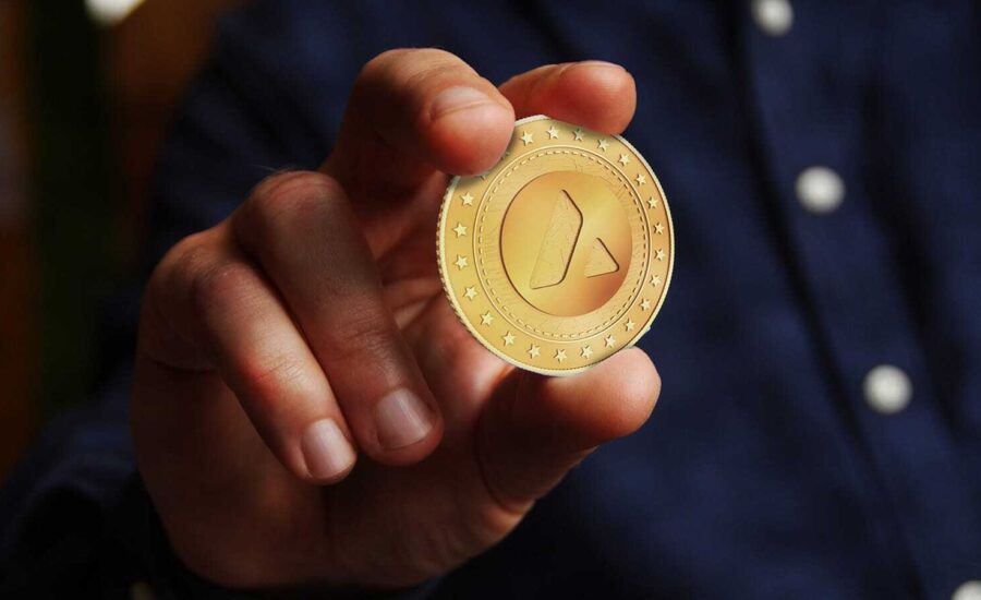 A hand holds out a gold coin with the triangular Avalanche logo