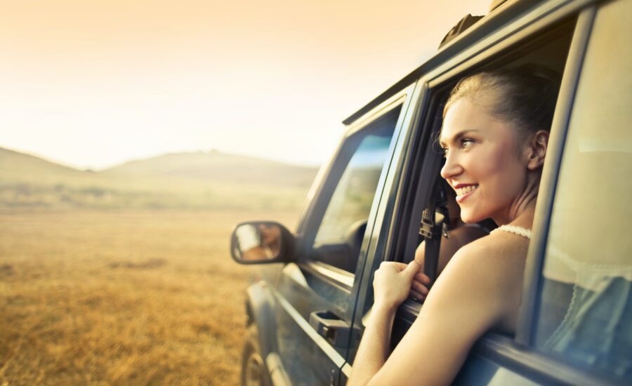 A smiling woman looks out the window of a jeep at a grassy plain