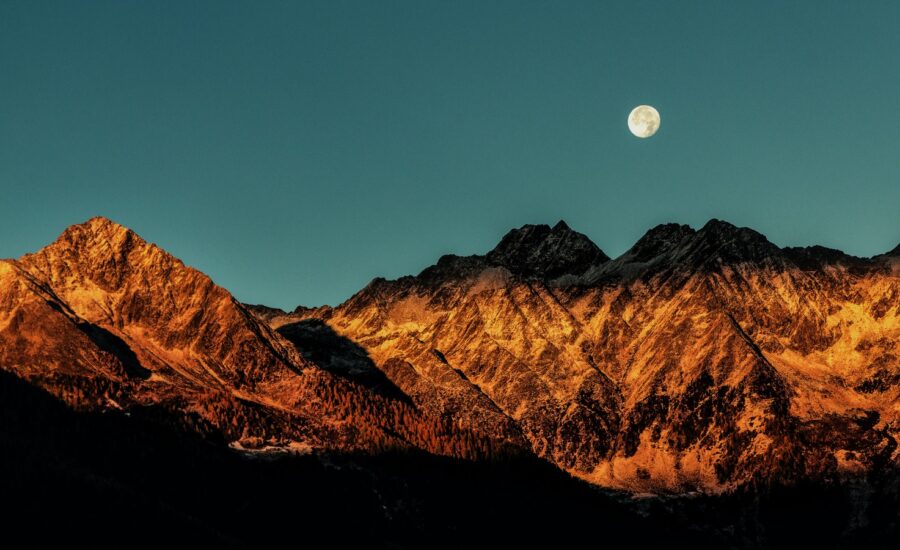 The moon rises over a snowy mountain range.