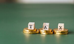 Three wood blocks spelling TAX sit on piles of gold coins