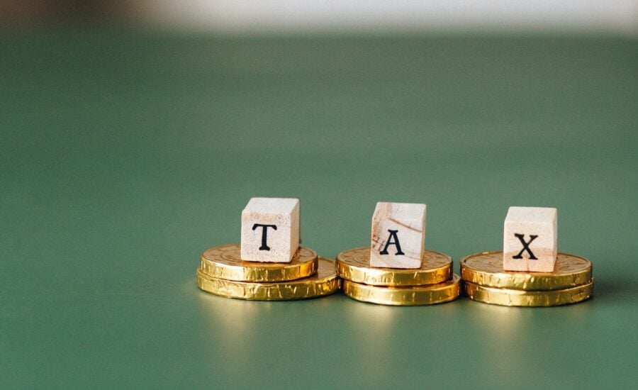 Three wood blocks spelling TAX sit on piles of gold coins