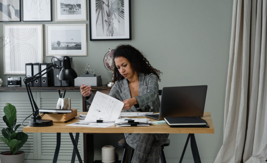 A woman is sitting at her desk at home, going through her bills to add them up.